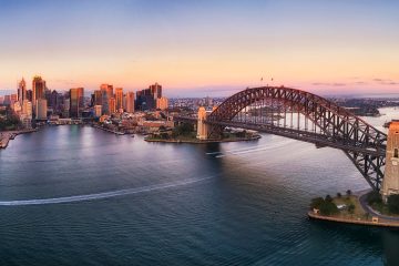 Colourful sky over Sydney city CBD high-rise towers at sunrise around Sydney harbour and the Sydney Harbour bridge in elevated aerial panorama.