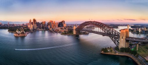 Colourful sky over Sydney city CBD high-rise towers at sunrise around Sydney harbour and the Sydney Harbour bridge in elevated aerial panorama.